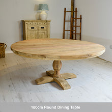 Load image into Gallery viewer, 180cm round reclaimed teak dining table in a room with a lamp and cabinet.