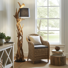 Load image into Gallery viewer, Wooden floor lamp next to a wicker chair with cushions in a room with a large window.