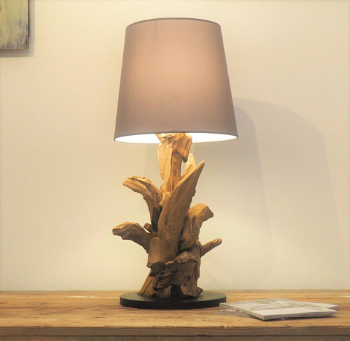 A table lamp with a unique design, featuring a reclaimed teak root base and a grey lampshade, placed on a wooden surface.