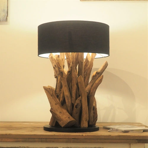 A rustic wooden root table lamp with a black lampshade, placed on a wooden table.