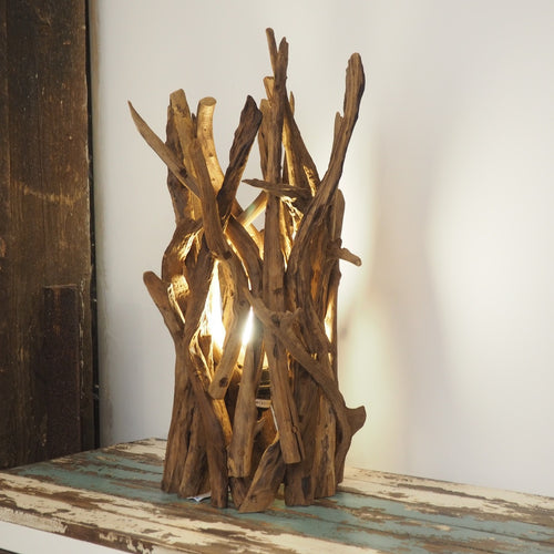 A rustic wooden spotlight lamp made from teak root, with the light on and illuminating the textured wood.