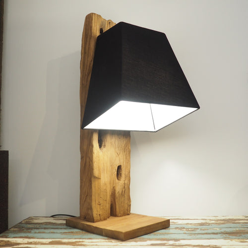 Reclaimed wood table lamp with characterful base showing original features of the timber. Shown with a black lampshade on a wooden table and a plain background.